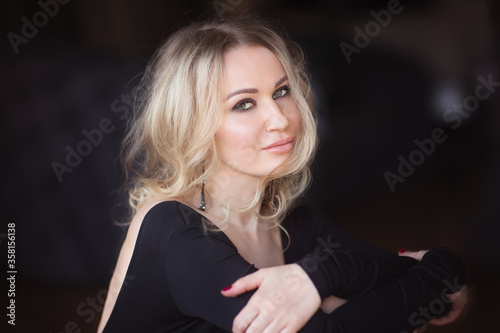 Portrait of young blond haired woman in black blouse. Black background with copy space
