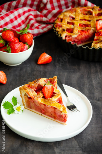 Pie with rhubarb and strawberries on a dark wooden background with fresh strawberries. Vertical orientation, copy space.