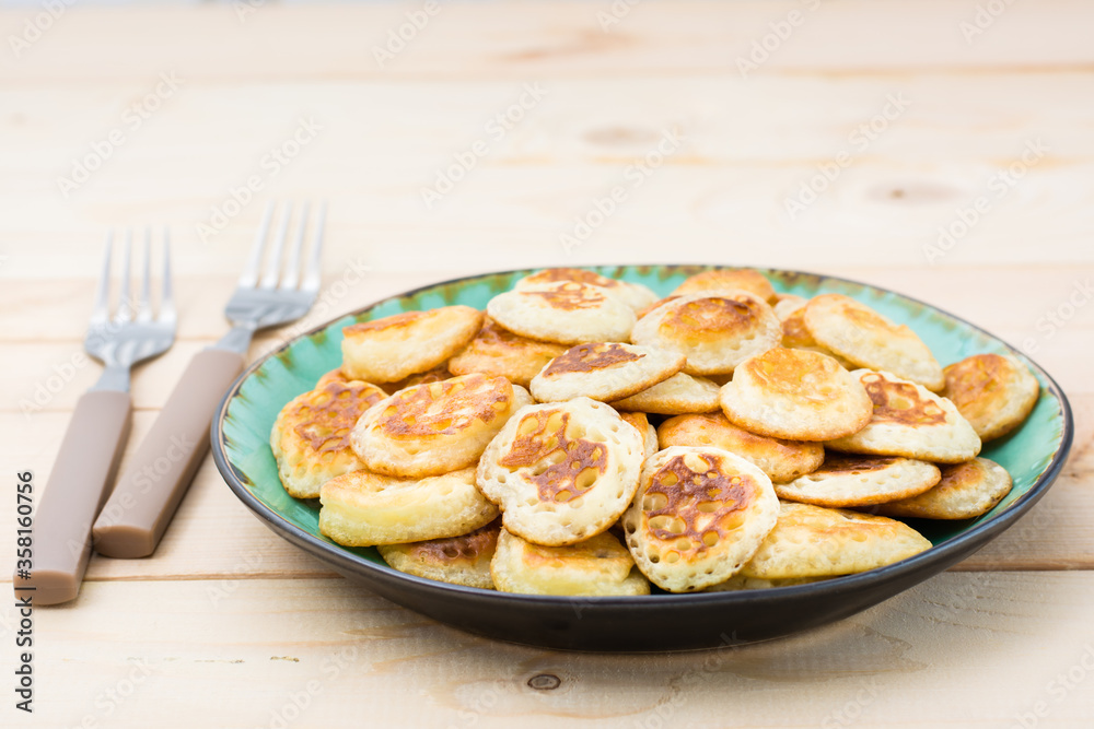 Trend breakfast. Dutch mini pancakes on plate and two forks on a wooden table. Trend breakfast. Dutch mini pancakes on plate and two forks on a wooden table.