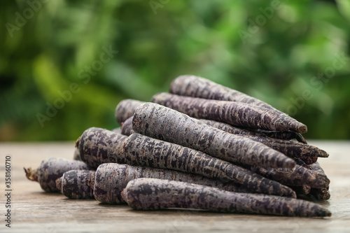 Raw black carrots on wooden table against blurred background