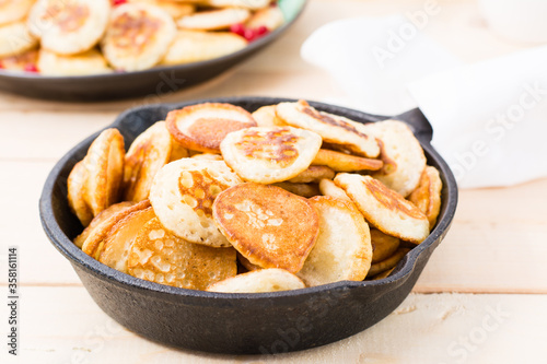 Trend breakfast. Dutch mini pancakes in a pan close-up on a wooden table.