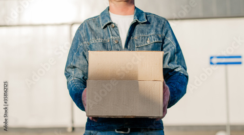 Courier in a face mask with a box in his hands. Portrait from the waist up. Delivery man concept.. Outdoor.
