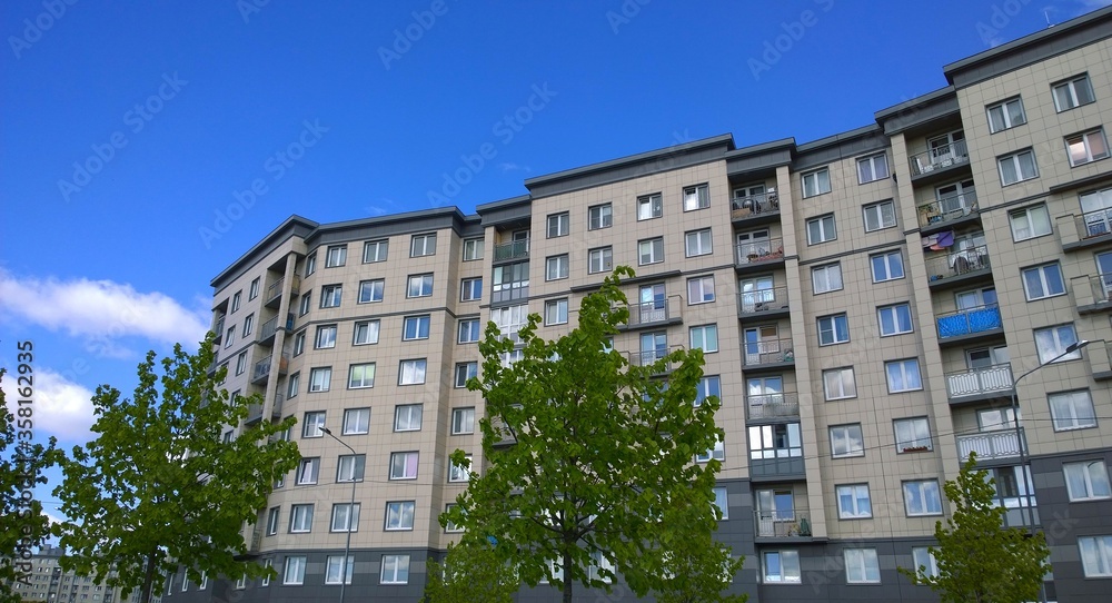 Facade of a new multi-story residential building. Sale and rental of economy class apartments and comfortable housing for young families. Cityscape. City living. Real estate. Blue sky. Green tree.
