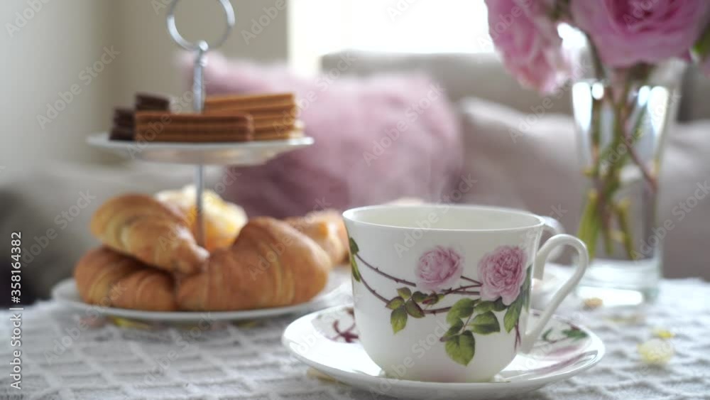 Afternoon tea with cup of tea, croissants, crackers and biscuits on hight tea stand in pink pastel. Cozy sence of afternoon party in conservatory room