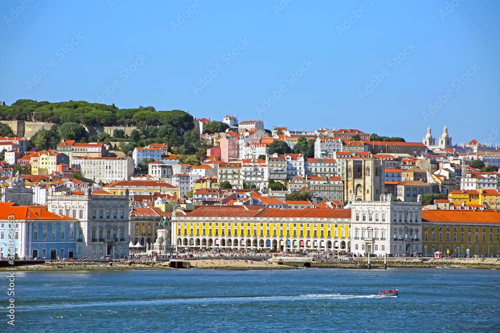 Multi coloured buildings of the old city of Lisbon. São Jorge Castle looking down on the city Praça do Comércio town square in the foreground. View from across the Tagus Estuary, Portugal.