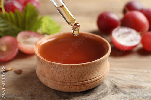 Dripping natural grape seed oil into bowl on wooden table, closeup. Organic cosmetic