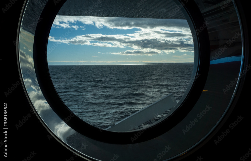 Sea view through the porthole of a passenger ferry in cloudy, calm weather