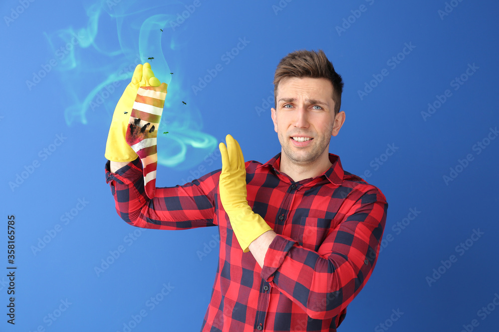 Displeased man with dirty smelly sock on color background Displeased man with dirty smelly sock on color background