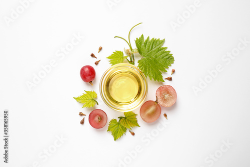 Composition with bowl of natural grape seed oil on white background, top view. Organic cosmetic photo