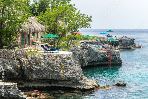 A unique location/ setting on the cliffs of Negril in Westmoreland, Jamacia. Famous vacation spot with seaside scenic views on the island coast. Thatch roof huts/ cottages, outdoor lounge chairs. photo