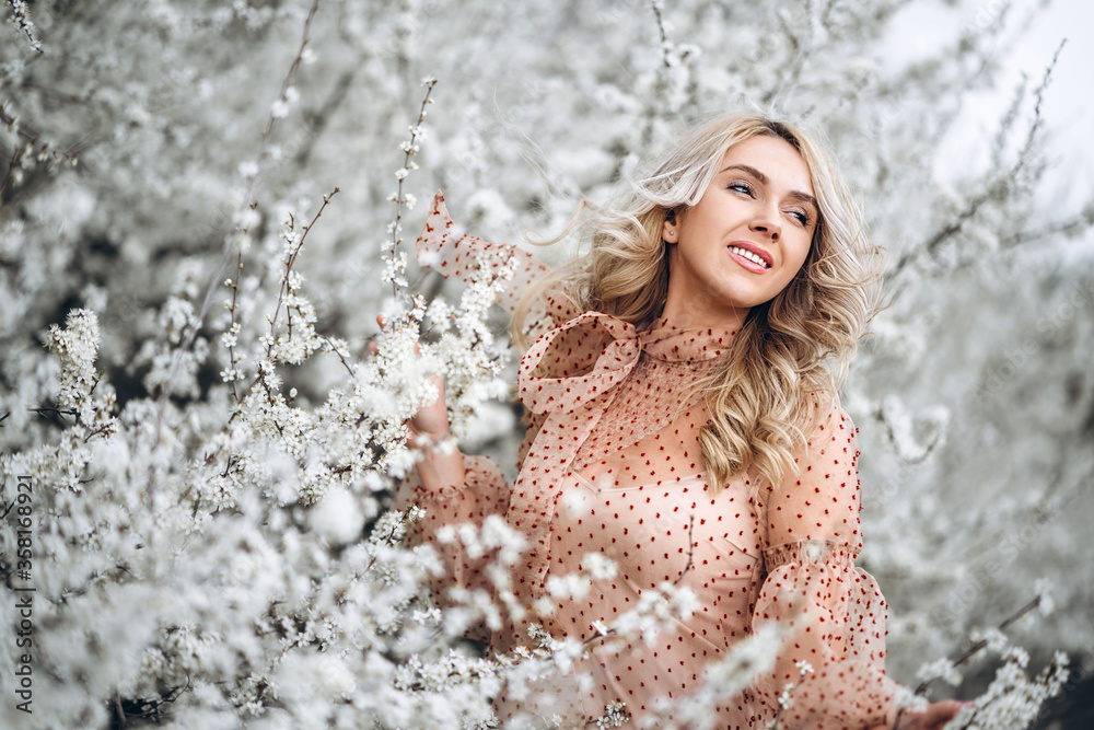 Woman with gorgeous smile, curly blond hair in red dress having fun in blooming garden Woman with gorgeous smile, curly blond hair in red dress having fun in blooming garden
