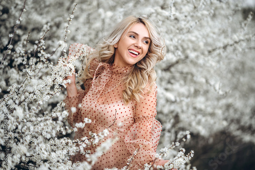 Woman with gorgeous smile  curly blond hair in red dress having fun in blooming garden