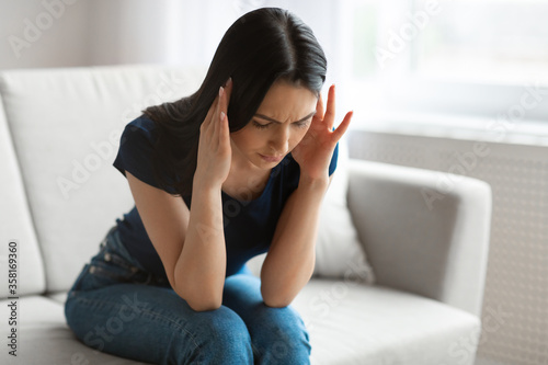 Woman Having Headache Suffering From Pain Sitting On Sofa Indoor