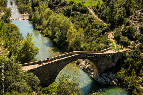 RODELLAR, HUESCA, SPAIN. Two mountain bikers ride across a narrow roman bridge over the River Alcanadre in the Sierra de Guara region. Photo: Victor Lucas