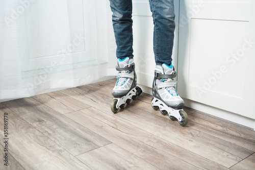 Two legs with jeans in roller skates standing at home on floor. Woman doing active sport at home in new equipment. Copy space