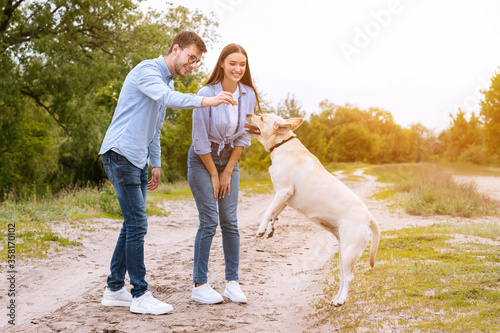 Young couple giving a treat to their happy dog © Prostock-studio
