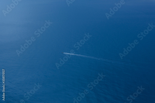 A lone boat in the endless blue sea. Top view of the sea background with the ship. The concept of summer vacation. Tourist destination. Sea tour. Pleasure boat view from above. © Anna Pismenskova