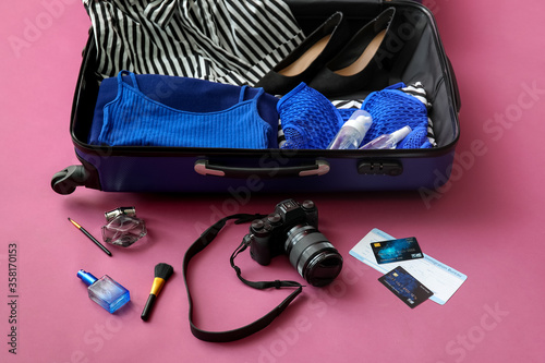 Open packed suitcase and accessories on color background