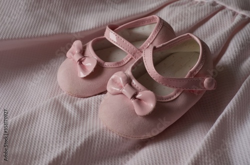 Pink baby shoes with bowknot on pink fabric background. Stylish baby shoes
