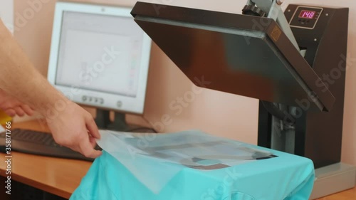 Heat press machine with t-shirt on wooden table. Worker presses a hand press to apply numbers to a high temperature T-shirt photo