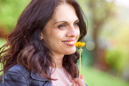 Middle-age woman in black leather jacket smiling, enjoying life, smelling flower photo