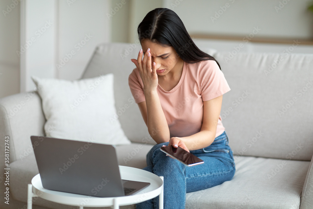 Frustrated Woman At Laptop Holding Phone Sitting On Sofa Indoor Frustrated Woman At Laptop Holding Phone Sitting On Sofa Indoor