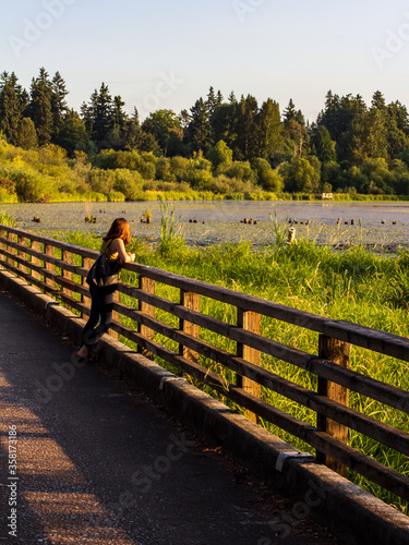 August 1, 2019 - Juanita Bay Park, Kirkland, Washington, USA - A woman looks out on Juanita Bay nature park while leaning agains a wood railing