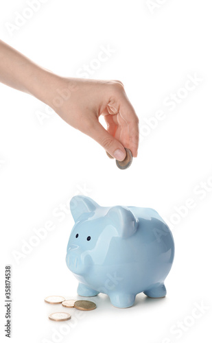 Woman putting money in piggy bank on white background