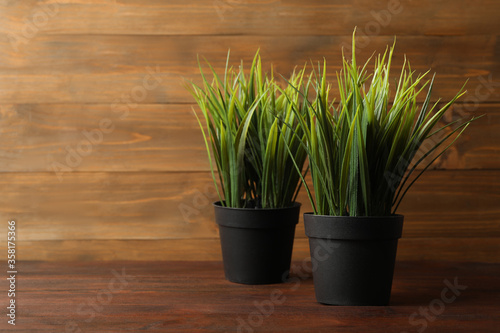 Artificial plants in dark flower pots on wooden table