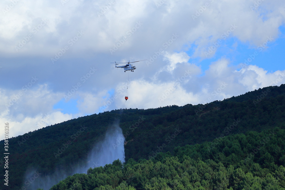 Firefighting helicopter intervenes for the fire that starts on the forest-covered mountain.