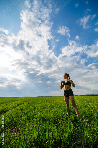 Healthy lifestyle concept. Young attractive woman in sportswear does stretching her hand before training on the nature against a blue sky. Muscle warming