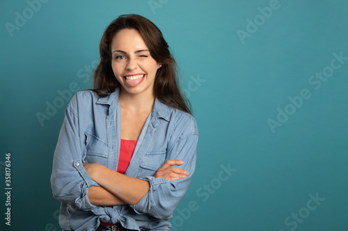 Fotografi mischievous and smiling young woman with folded arms on blue background