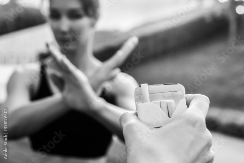 young woman refuses cigarettes. shows with hands a stop symbol. hand holds out her cigarettes. smoking cessation concept. healthy lifestyle. black and white photo