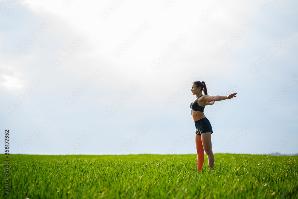 Attractive girl athlete does warm-up outdoors, exercises for muscles. Young woman go in for sports, healthy lifestyle, athletic body. She is in sportswear, black top and shorts Attractive girl athlete does warm-up outdoors, exercises for muscles. Young woman go in for sports, healthy lifestyle, athletic body. She is in sportswear, black top and shorts