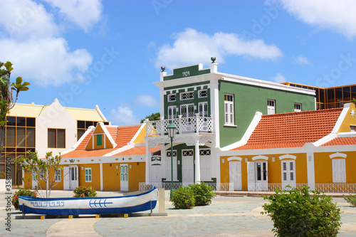 Several colored buildings stand on the street. The sun shines brightly, the sky is blue. In the foreground on the ground is a white-blue boat. Aruba August 2014 photo