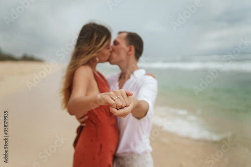 Beautiful engagement ring and a young couple by the ocean