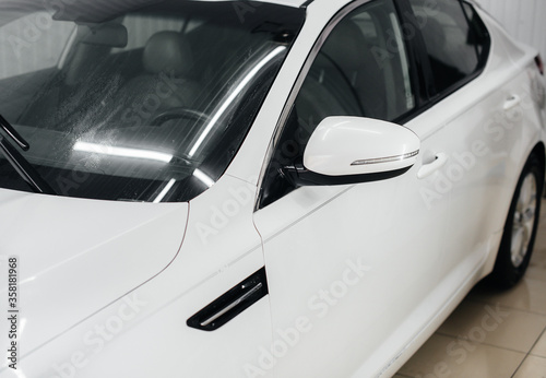 Modern washing with foam and high-pressure water of a white car. Car wash