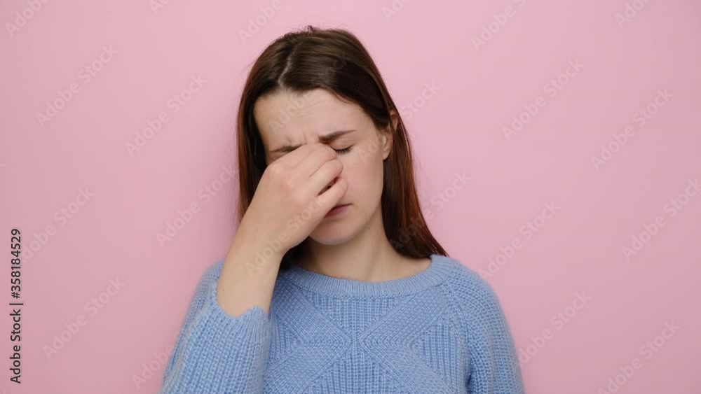 Sad tired of glasses young woman massaging nose bridge, feeling eye strain, exhausted lady suffering from headache or migraine, wears blue sweater, isolated on pink background. Eyes fatigue concept Sad tired of glasses young woman massaging nose bridge, feeling eye strain, exhausted lady suffering from headache or migraine, wears blue sweater, isolated on pink background. Eyes fatigue concept