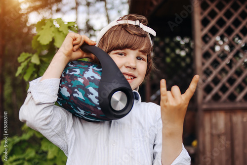 Child with portable speaker enjoying the music in park, outdoors. Kid listening music by wireless acoustic column at nature. Boy on vacation with music.
