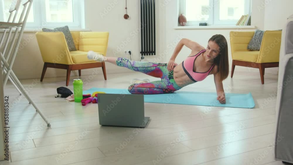 Young fit woman doing workout with online trainer using laptop at home building strong core focused and motivated close up slow motion Young fit woman doing workout with online trainer using laptop at home building strong core focused and motivated close up slow motion