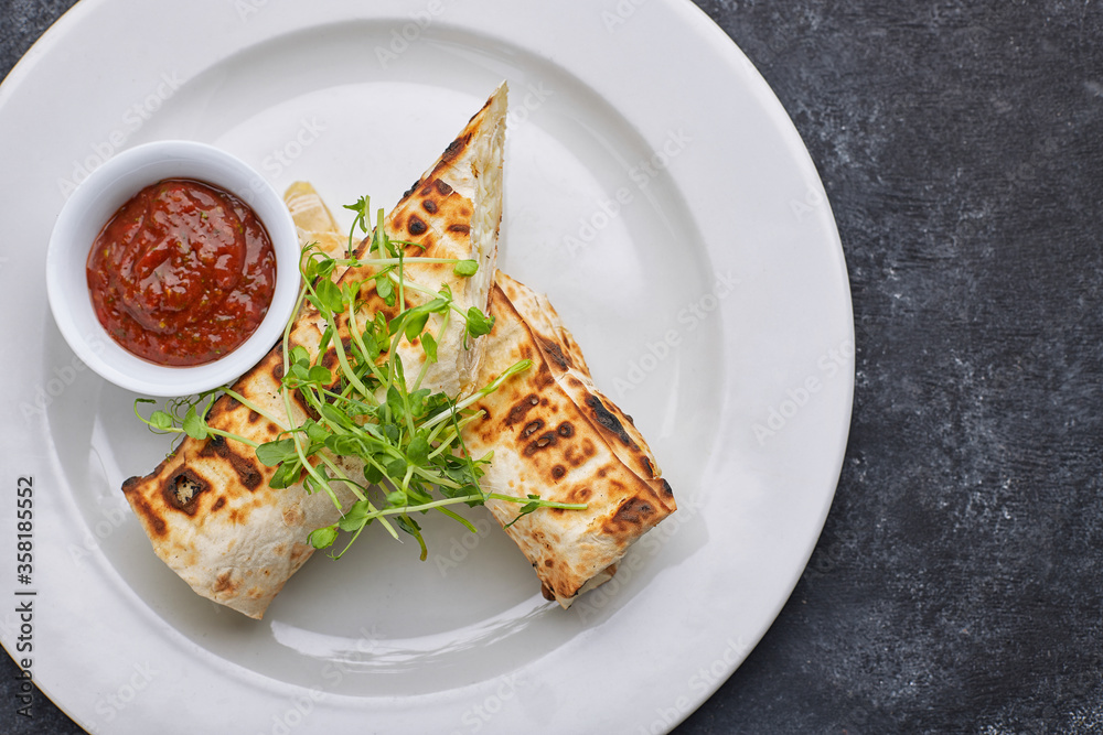 Pita bread with suluguni cheese, sauce, microgreen, on a white plate, on dark concrete. Cooked on the grill