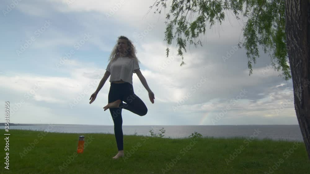 Back view of young fit woman practice yoga on coast near the lake or sea. Woman doing Standing Half Lotus pose Back view of young fit woman practice yoga on coast near the lake or sea. Woman doing Standing Half Lotus pose