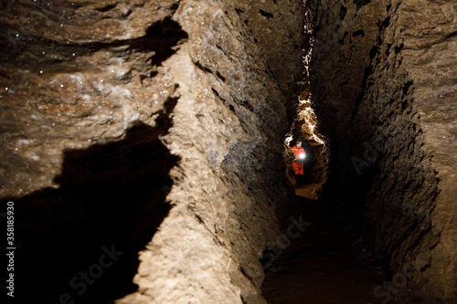 Man walking and exploring dark cave with light headlamp underground. Mysterious deep dark, explorer discovering mystery moody tunnel looking on rock wall inside. photo