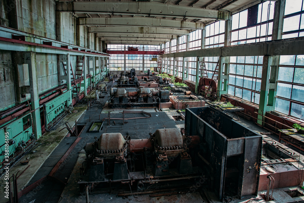 Old abandoned overgrown factory with rusty remains of industrial machinery in workshop