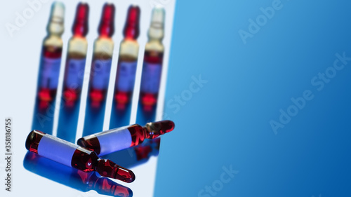 Seven medical bottles with red liquid in light with a blue shadows and reflection. Blue gradient copy space