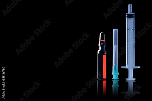 A medical ampoule with red liquid, a needle and a syringe in a side lit with reflection isolated on black