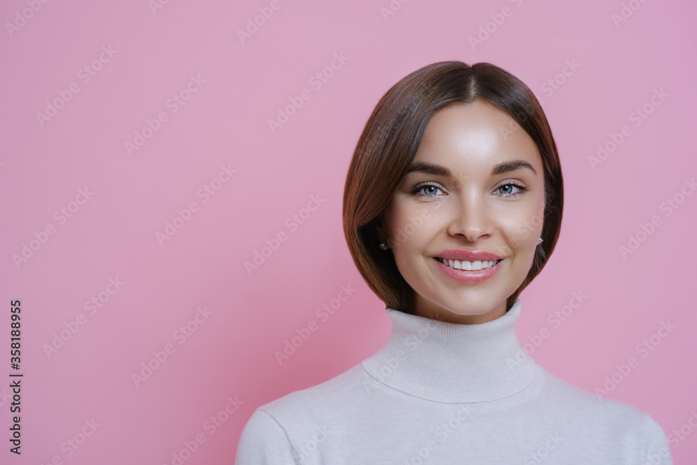 Close up portrait of lovely satisfied joyful woman with dark hair, smiles pleasantly, shows white teeth, wears poloneck, isolated on pink background, empty space for your advertising content. Close up portrait of lovely satisfied joyful woman with dark hair, smiles pleasantly, shows white teeth, wears poloneck, isolated on pink background, empty space for your advertising content.