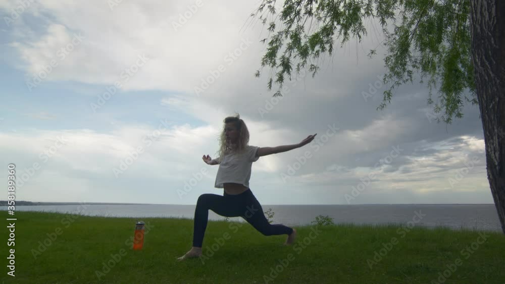 Young fit woman practice yoga on coast near the lake or sea. Woman doing Warrior one and two Poses Young fit woman practice yoga on coast near the lake or sea. Woman doing Warrior one and two Poses