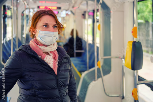 Redhead woman in medical mask rides on a bus, close up. Problems of travel in transport during the coronavirus epidemic