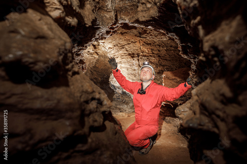 Man walking and exploring dark cave with light headlamp underground. Mysterious deep dark, explorer discovering mystery moody tunnel looking on rock wall inside. photo